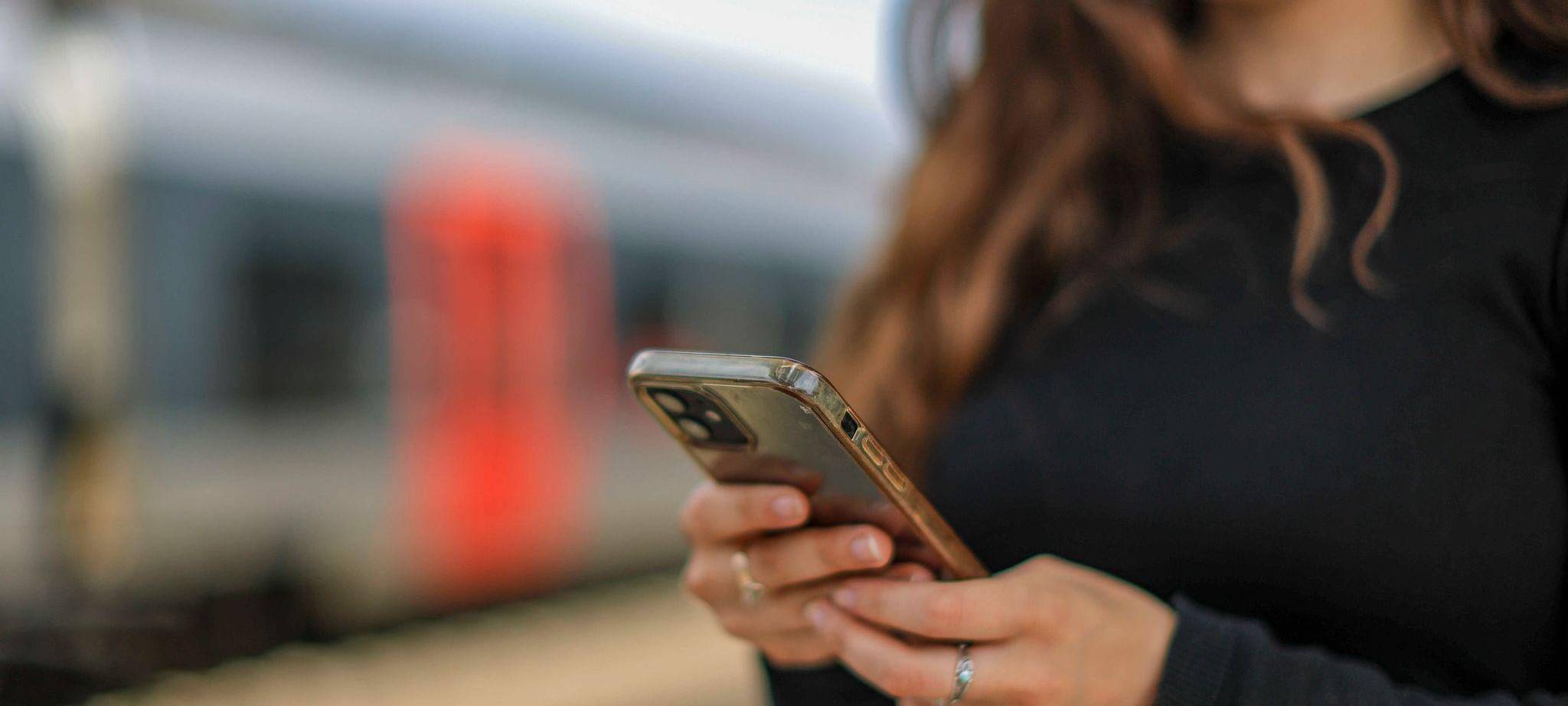 Eine junge Frau steht mit ihrem Mobiltelefon auf einem Bahnsteig
