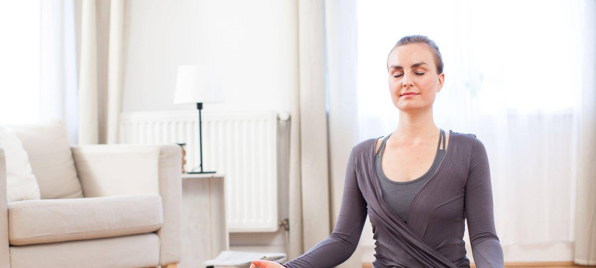 Eine junge Frau sitzt im Schneidersitz zuhause und macht Yoga