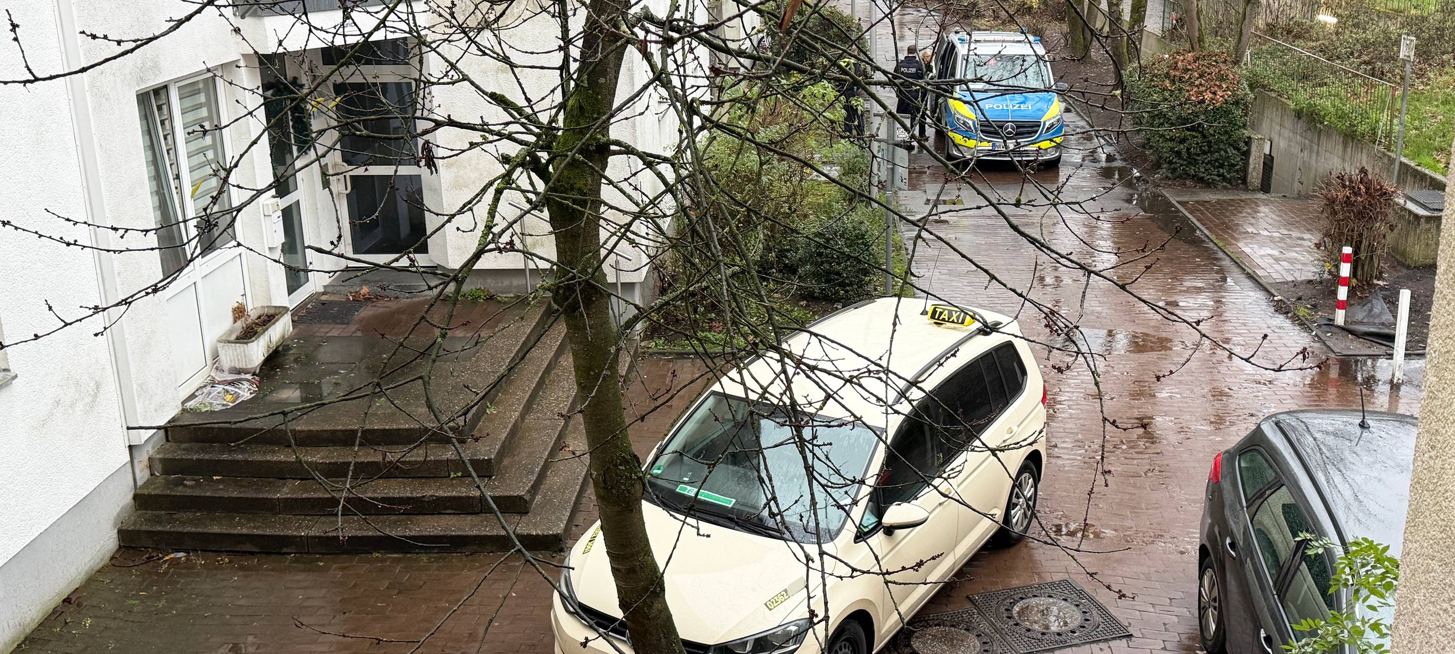 Ein Taxi steht auf einem Gehweg in einem Wohngebiet, dahinter ein Polizeiwagen.
