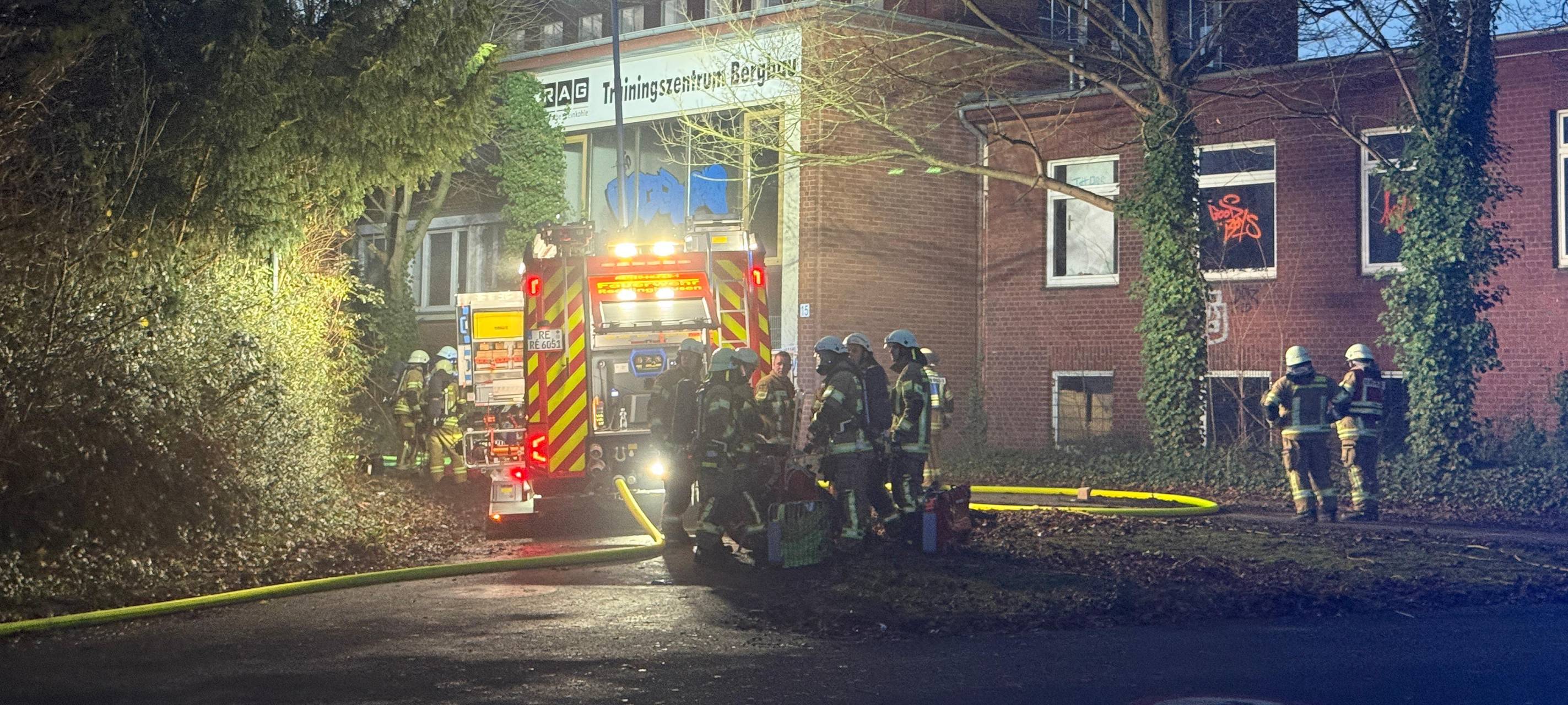 Ein Feuerwehrauto und mehrere Feuerwehrleute stehen vor dem verrauchten Eingang des alten Bergbauberufskollegs in Recklinghausen