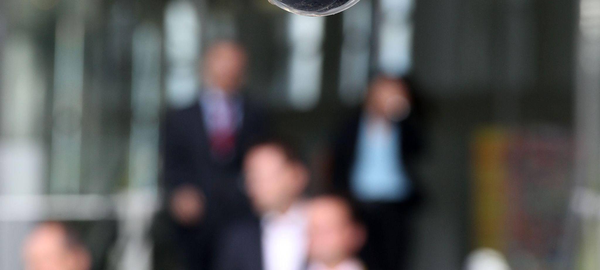 Mitarbeiter laufen unter einer Überwachungskamera entlang