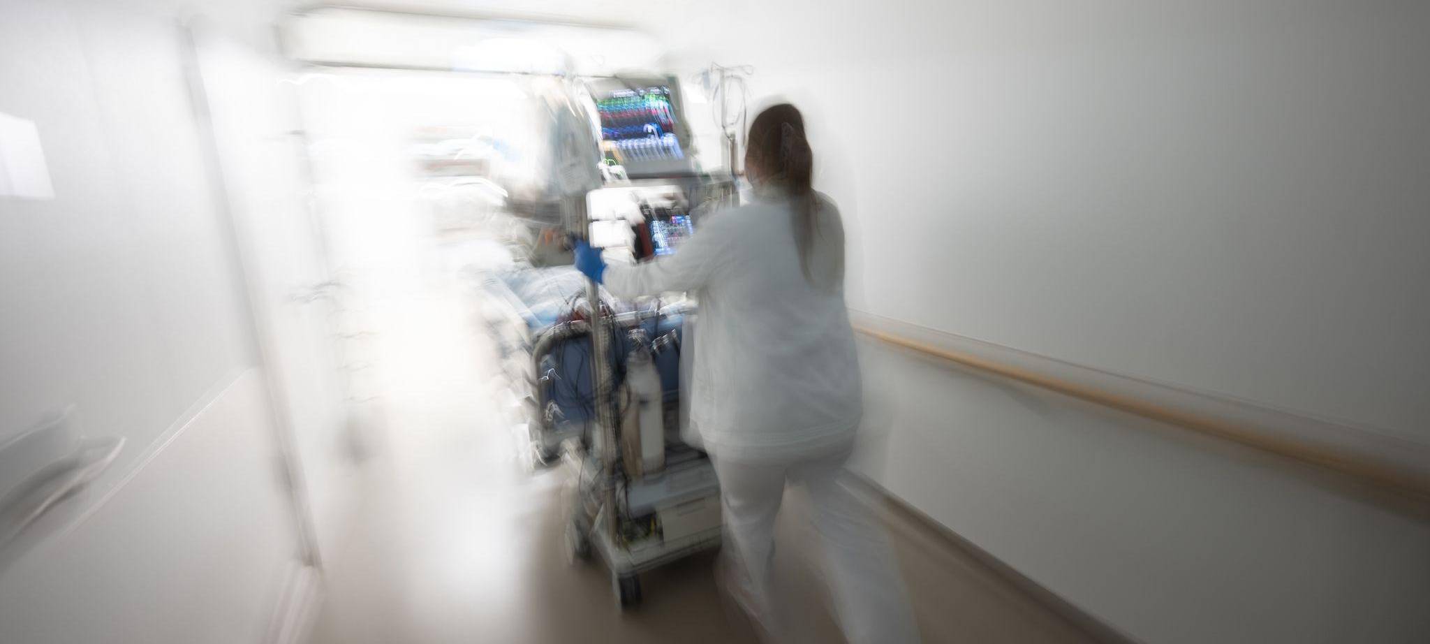 Pflegerin fährt eine Intensivpatientin durch denGang einer Klinik