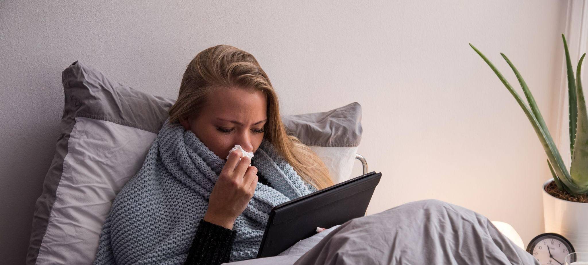 Eine Frau mit Tablet liegt krank im Bett