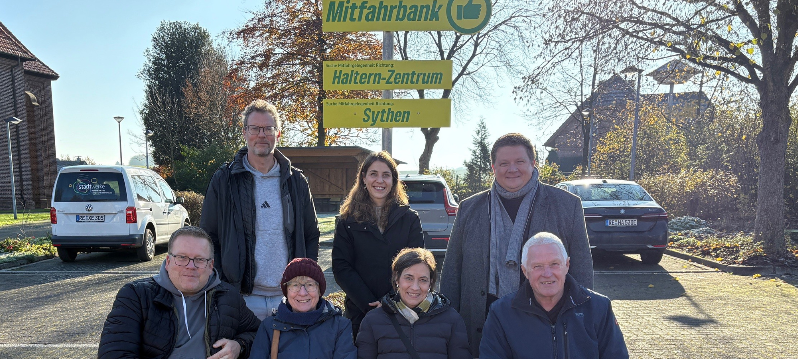 Mehrere Menschen sitzen auf einer Bank in Haltern-Lavesum, darüber ein Schild mit der Aufschrift "Mitfahrbank"